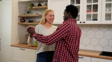 Birbirlerine aşık çok ırklı bir çift ev mutfağında slow dans dinliyorlar.
