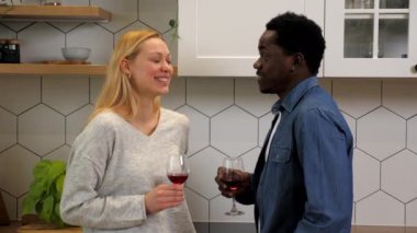 Gülümseyen çok ırklı aile aşıkları mutfakta bir bardak kırmızı şarapla konuşuyor.