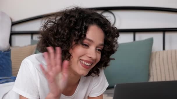 Smiling curly woman uses laptop greets talking listens fiends online video call — Vídeo de Stock