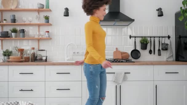 Felice donna riccia ispanica ascoltando musica e ballando a casa in cucina — Video Stock
