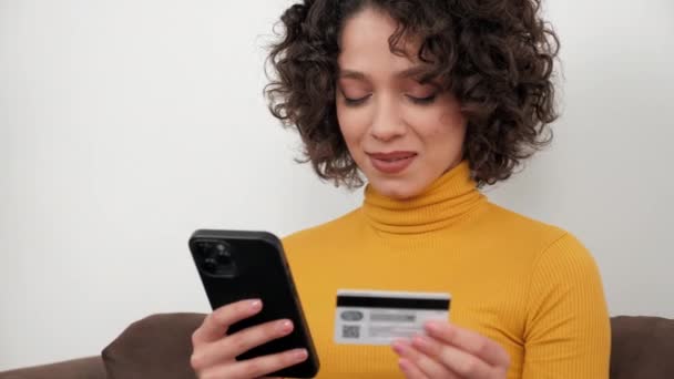 女性はスマートフォン経由でオンラインショッピングにギフトを支払うためにクレジットカードコードを入力します — ストック動画