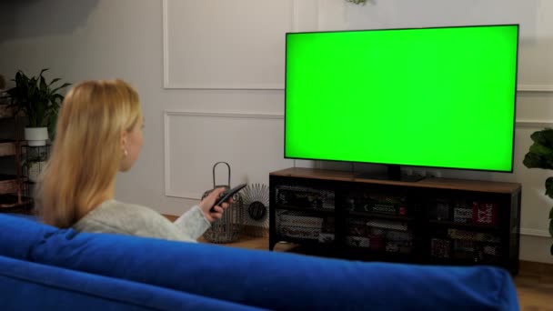 Женщина смотрит на зеленый экран телевизор хрома ключ макет дисплей переключения каналов — стоковое видео