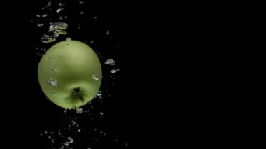 Slow motion one green apple spinning falling into transparent water on black background. Beautiful fresh fruit splashing in aquarium. Organic fruits, healthy food, diet, air bubbles