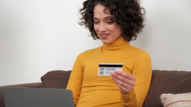 Gülümseyen kıvırcık kadın müşteri hediye ödemek için kredi kartı koduna giriyor, bilgisayarla online alışveriş yapıyor. Evde bilgisayar yoluyla İspanyol kadın alışverişi ya da ödemeler var. Çevrimiçi bankacılık