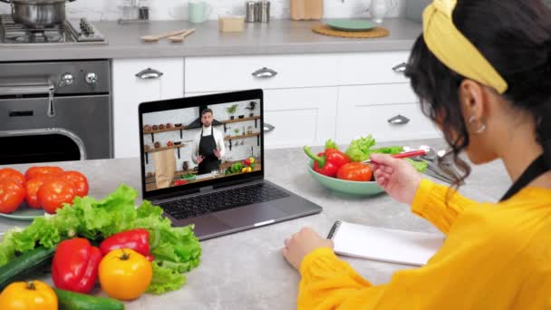 厨房里的女人在网上学习视频摄像头聊天笔记本电脑 听老师在笔记本里写烹饪菜谱 电脑屏幕上的男性厨师食物博客教授家庭主妇烹饪课 — 图库视频影像