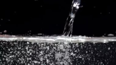 Akvaryumda yavaş hareket eden su akıntısı siyah bir zemine düşer. Yavaş çekim kristal berrak su akışı yüzeye çarpar ve hava kabarcıkları yaratır.