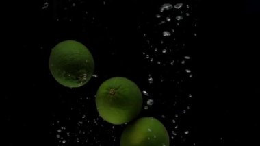 Yavaş çekim üç kireç siyah arkaplanda şeffaf suya düşüyor. Akvaryuma taze meyve sıçraması. Citrus, yemek, hava kabarcıkları