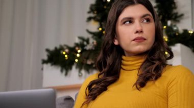 Thoughtful businesswoman uses laptop distance works for computer typing on keyboard sitting on couch at cozy home. Thinking woman online chatting with best friends. Christmas, New Year winter holidays