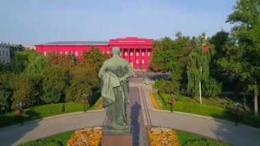 Aerial view back view statue of the writer Taras Grigorovich Shevchenko in park on a sunny spring day. Drone shot red building facade Kyiv National University of Taras Shevchenko. Capital of Ukraine