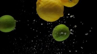 Yavaş çekim sarı limon ve yeşil kireç siyah arkaplanda şeffaf suya düşüyor. Akvaryuma taze meyve sıçraması. Citrus, yemek, hava kabarcıkları