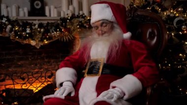 Noel Baba arka plandaki şömine ağacında otururken uyuyor. Yaşlı adam Noel Baba kostümü giymiş, uyuyakalıyor. Yeni yıl Noel kış tatili kutlaması