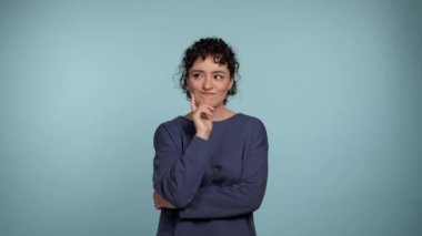 Mavi kazaklı düşünceli genç kıvırcık kadın etrafına bakıyor, hangi tarafı seçeceğini düşünüyor. İzole edilmiş açık mavi arka planda duran dalgın, güzel bir kadın. İnsanlar yaşam tarzı kavramını hisseder