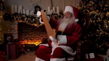 Noel Baba, Noel tatili için çocukların hediyelerini içeren bir mektup okuyor. Yaşlı büyükbaba Noel Baba kostümü giymiş arka plandaki şömine ağacında oturuyor. Yeni Yıl