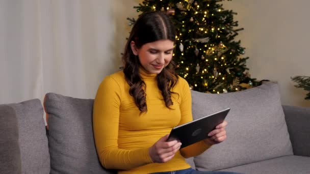 아름다운 게이머가 크리스마스 트리에 태블릿으로 온라인 게임을 있습니다 스웨터를 양성인 — 비디오
