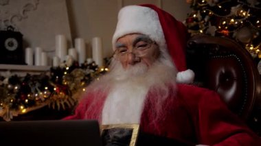 Modern gülümseyen Noel Baba çocukları internetteki webcam laptop görüntülü sohbetlerinde dinliyor. Noel Baba kostümü giymiş büyük baba uzaktan kumandalı sanal bağlantı. Yeni yıl, Noel