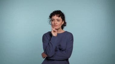 Mavi kazaklı düşünceli genç kıvırcık kadın etrafına bakıyor, hangi tarafı seçeceğini düşünüyor. İzole edilmiş açık mavi arka planda duran dalgın, güzel bir kadın. İnsanlar yaşam tarzı kavramını hisseder