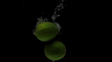 Yavaş çekim üç kireç siyah arkaplanda şeffaf suya düşüyor. Akvaryuma taze meyve sıçraması. Citrus, yemek, hava kabarcıkları