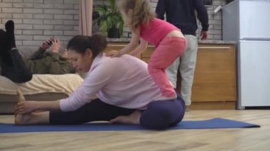 Bir anne evde, mutfakta küçük kızıyla yoga yapmaya çalışır. Evde çocuk ve aileyle spor ve spor. Coronavirus kilitlenmesi, sosyal uzaklık