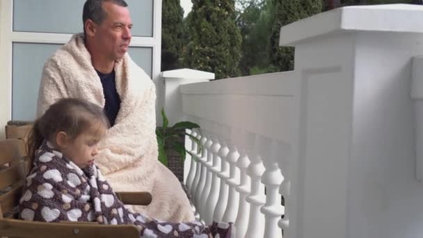 Far och dotter är bekvämt insvepta i en varm filt och sitter tillsammans på balkongen. Låsning karantän isolering stanna hemma under Covid-19 Coronavirus. Familjetidsfördriv och livsstil — Stockvideo