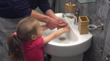 Baba ve kız ellerini lavabonun üzerinde sabunla yıkıyorlar. Kişisel temizlik ve el yıkama, koronavirüsü önleme. COVID-19 'a karşı dezenfeksiyon