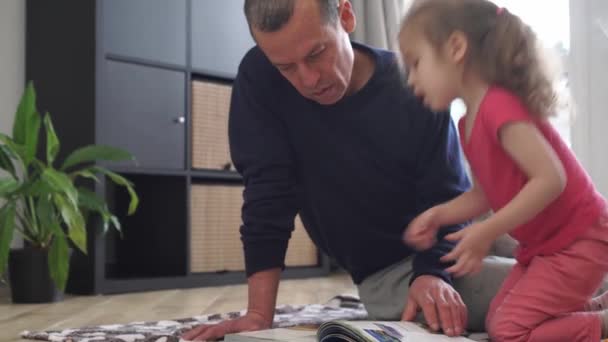 Ένας πατέρας διαβάζει ένα βιβλίο σε ένα παιδί. Χαρούμενη Ημέρα Πατέρων. Εκπαίδευση, χόμπι, έννοια οικογενειακού ελεύθερου χρόνου. Οικογένεια στο σπίτι μαζί κατά τη διάρκεια του αποκλεισμού Covid-19 — Αρχείο Βίντεο