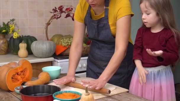 The child kneads and rolls out the dough. Happy daughter is helping mother to prepare traditional festive pumpkin pie for Thanksgiving dinner. American family celebrates Thanksgiving. Fall home decor — Stock Video