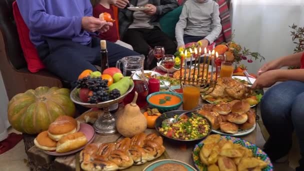 Authentieke Joodse familie viert Chanoeka avond en dineert samen thuis. Traditioneel koosjer eten en drinken op de feestelijke tafel. Menorah met brandende kaarsen — Stockvideo