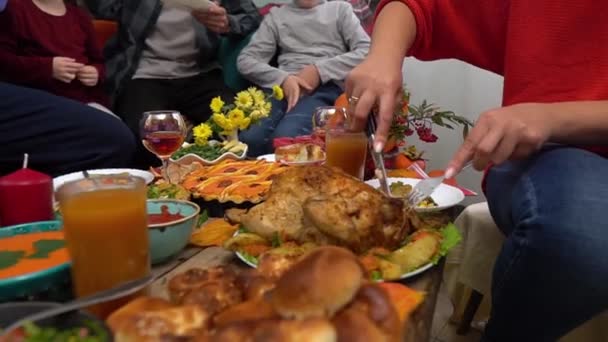 Hálaadási vacsora. Egy boldog többnemzetiségű család gyerekekkel egy ünnepi asztalnál. Anya pulykát vág. Hagyományos ételek az asztalon - sütőtök pite, sült burgonya, zsemle, zöldbab, kukorica — Stock videók