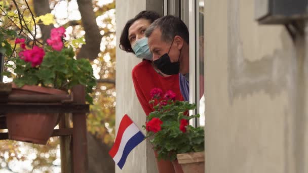 Blocco di Covid-19 nei Paesi Bassi. Triste coppia olandese sul balcone di casa. Bandiera dei Paesi Bassi. Auto-isolamento in quarantena, isolamento, stare a casa, distanza sociale — Video Stock