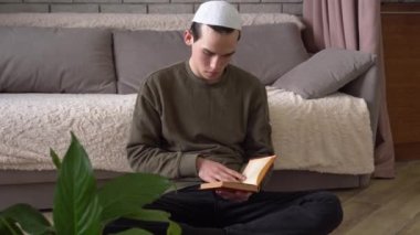 Müslüman öğrenci evde yerde oturmuş kitap okuyor. Geleneksel Dini Eğitim Okulu, Uzaktan Öğrenme, Tecrit. Genç adam ders çalışıyor.