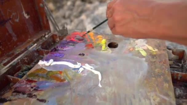 De kunstenaar mengt olieverf op het palet met een paletmes. Kunsttherapie. Schilderen in natuur, landschap — Stockvideo