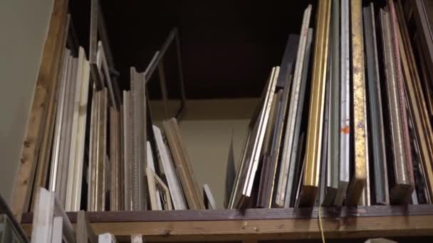 A shelf rack with paintings in artist studio. Old canvases and frames on a shelf in the artists studio — Stock Video