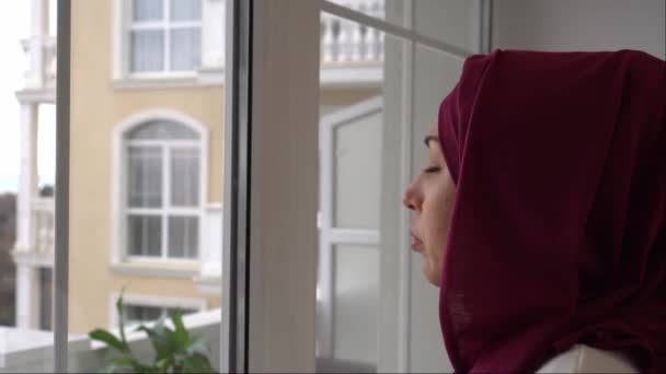 Verrouillage, ordre de rester à la maison. Triste adulte seule femme musulmane dans le hijab regarde la ville par la fenêtre. Rester à la maison, auto-isolement, quarantaine pendant la Covid-19 — Video