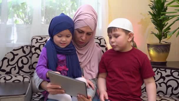 Fjärrundervisning på nätet för barn. Glad traditionell muslimsk familj, mamma i hijab och barn tillsammans hemma med hjälp av en surfplatta samtal till läraren under Covid-19 lockdown — Stockvideo