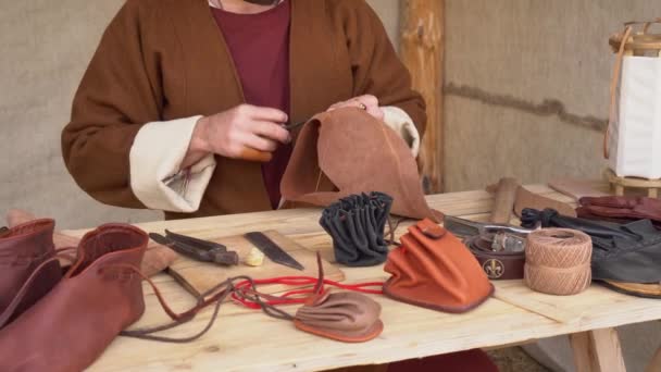 Historical European Leather workshop. Medieval leatherworker craftsmen. Craftsman sews by hand a wallet, shoes, belt, gloves — Wideo stockowe