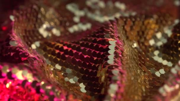 La textura de la tela para una fiesta con lentejuelas de oro de cerca. Luces de colores neón y bokeh. Antecedentes de las vacaciones — Vídeo de stock