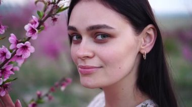 Genç, güzel ve seksi bir kızın portresi. Bahçede bahar çiçekleri. Narin pembe çiçekli meyveli şeftali dalı