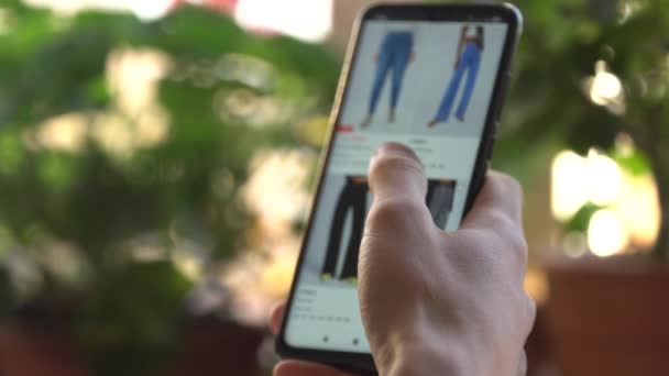 Eine Frau zu Hause kauft im Internet-Shop mit dem Smartphone ein. Der Kunde bestellt Jeans in einem Online-Geschäft per Smartphone. Online-Einkauf — Stockvideo