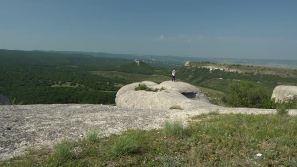 Женщина-туристка в горах. Взрослая женщина стоит на краю скалы и смотрит на небо с поднятыми руками — стоковое видео