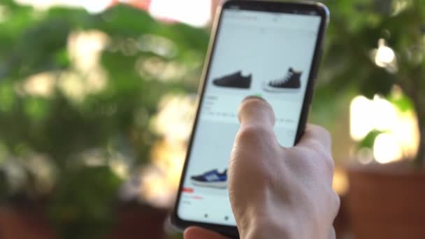 Um homem em casa usando Smartphone compra na Internet Shop. Encomendas de clientes sapatos em uma loja on-line usando um smartphone. Compras Online. — Vídeo de Stock