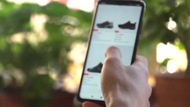 Ein Mann zu Hause kauft im Internet-Shop mit dem Smartphone ein. Der Kunde bestellt Schuhe in einem Online-Geschäft mit einem Smartphone. Online-Einkauf. — Stockvideo