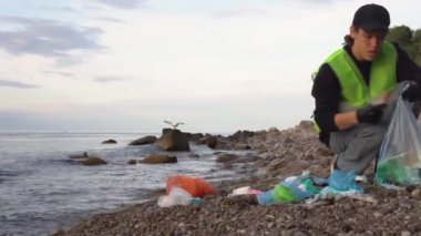 Coronavirus plastik atığı, kullanılmış yüz maskesi, okyanusta eldivenler. Çöp toplayıcısı ya da gönüllü, deniz kıyısını temizliyor. Çevre kirliliği. Yüksek kalite 4k görüntü