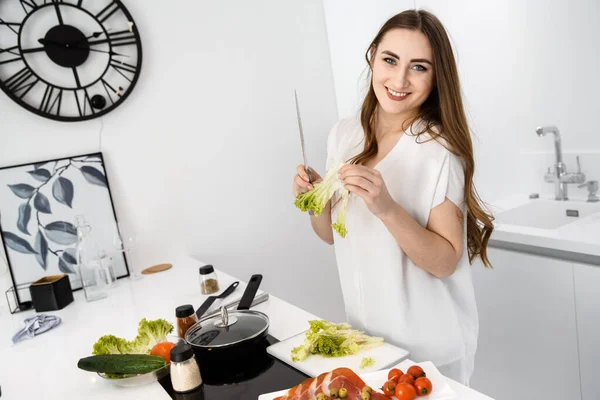 Genç, Güzel Kız Modern, Beyaz Mutfakta Kahvaltı Hazırlıyor. Omlet ve Baharatlı Sebzeler Tezgahta