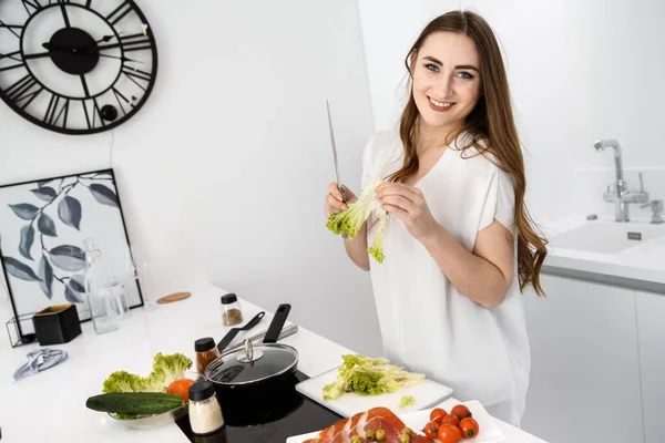 Giovane, Bella ragazza sta preparando la colazione in una moderna cucina bianca. Omelet e verdure stagionate sul piano di lavoro Immagini Stock Royalty Free