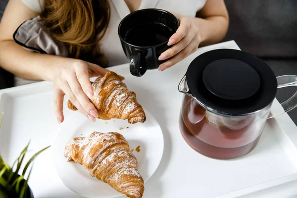 Una ragazzina fa colazione a letto. Croissant francesi con tè su un vassoio Foto Stock