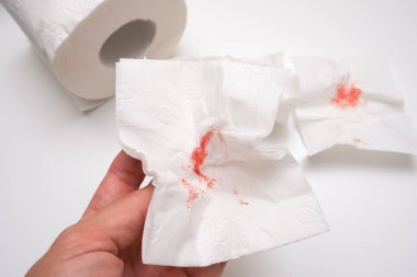 El ele tutuşan kanlı tuvalet kağıdı ve beyaz arka plan, basur ve rektal kanama kavramı.
