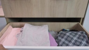 Kadın elleri bir çekmeceyi açar, giyinmek ve giyinmek için seçer ve soyunur, katlanmış giysiler organize olarak yatar.
