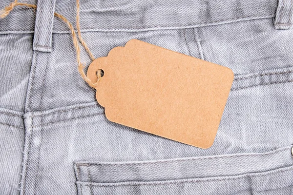 Craft prázdný štítek na šedé ošuntělé džíny pozadí, prodej a sleva koncept — Stock fotografie