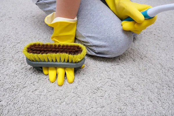 Ребенок в жёлтых резиновых перчатках очищает дом, ковер от пыли и пятен кистью — стоковое фото