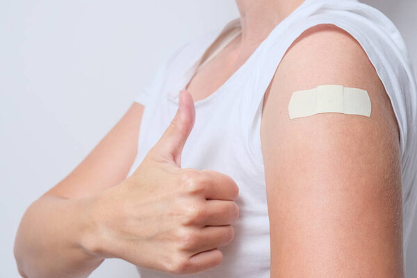 A woman showing thimb up and her arm with an adhesive bandage after injection of vaccine. Happy of getting vaccinated from corona virus, covid-19